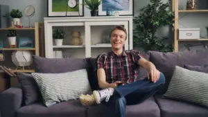 Veselý muž sedí na pohovce s popcornem a užívá si volný čas v stylovém obývacím pokoji.